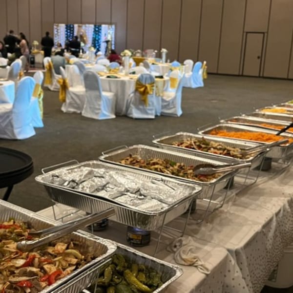 A long buffet line of Mexican food in aluminum trays, with a banquet hall in the background.