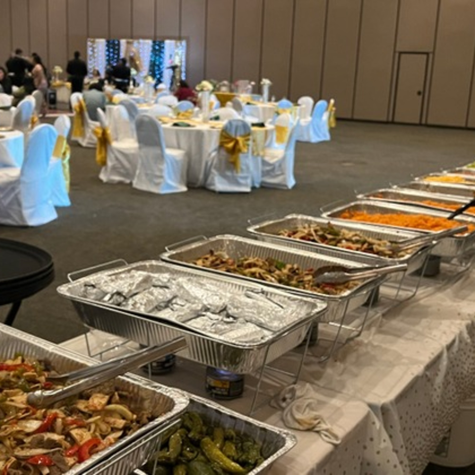A long buffet line of Mexican food in aluminum trays, with a banquet hall in the background.
