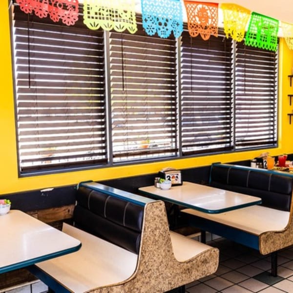 Interior of Taqueria Mexico Lindo with yellow walls, booths, and colorful papel picado banners.