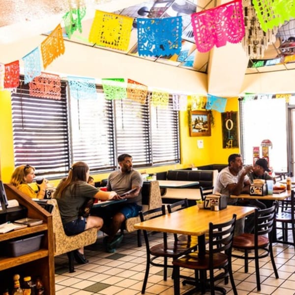 Customers seated at tables and booths in a brightly decorated Mexican restaurant with colorful papel picado.