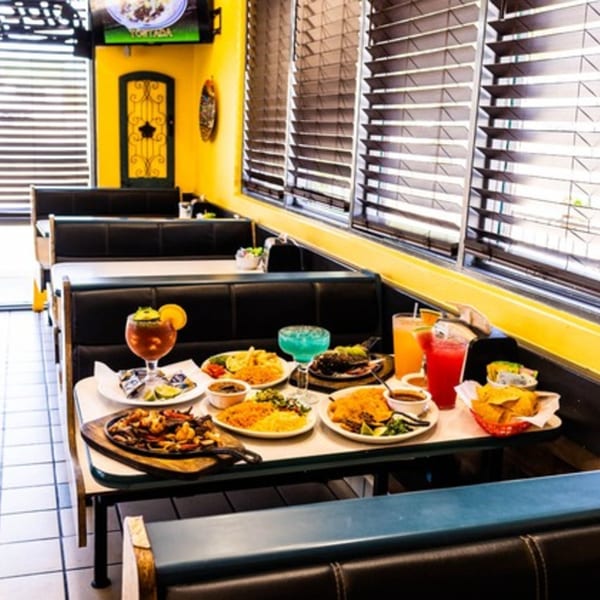 A table at Taqueria Mexico Lindo laden with various Mexican dishes and colorful drinks.