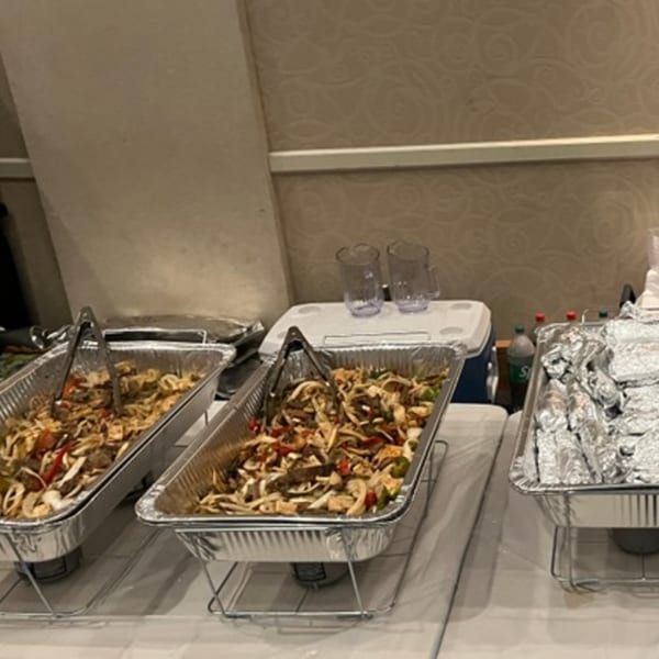 Mexican catering spread with two large foil pans of fajitas and a pan of foil-wrapped burritos.